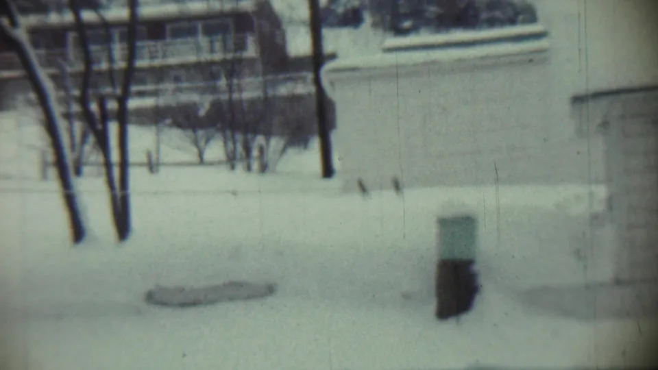 1959 Chadron, Nebraska 8mm frame showing a snowy residential yard with bare trees and neighboring building details in soft focus.
