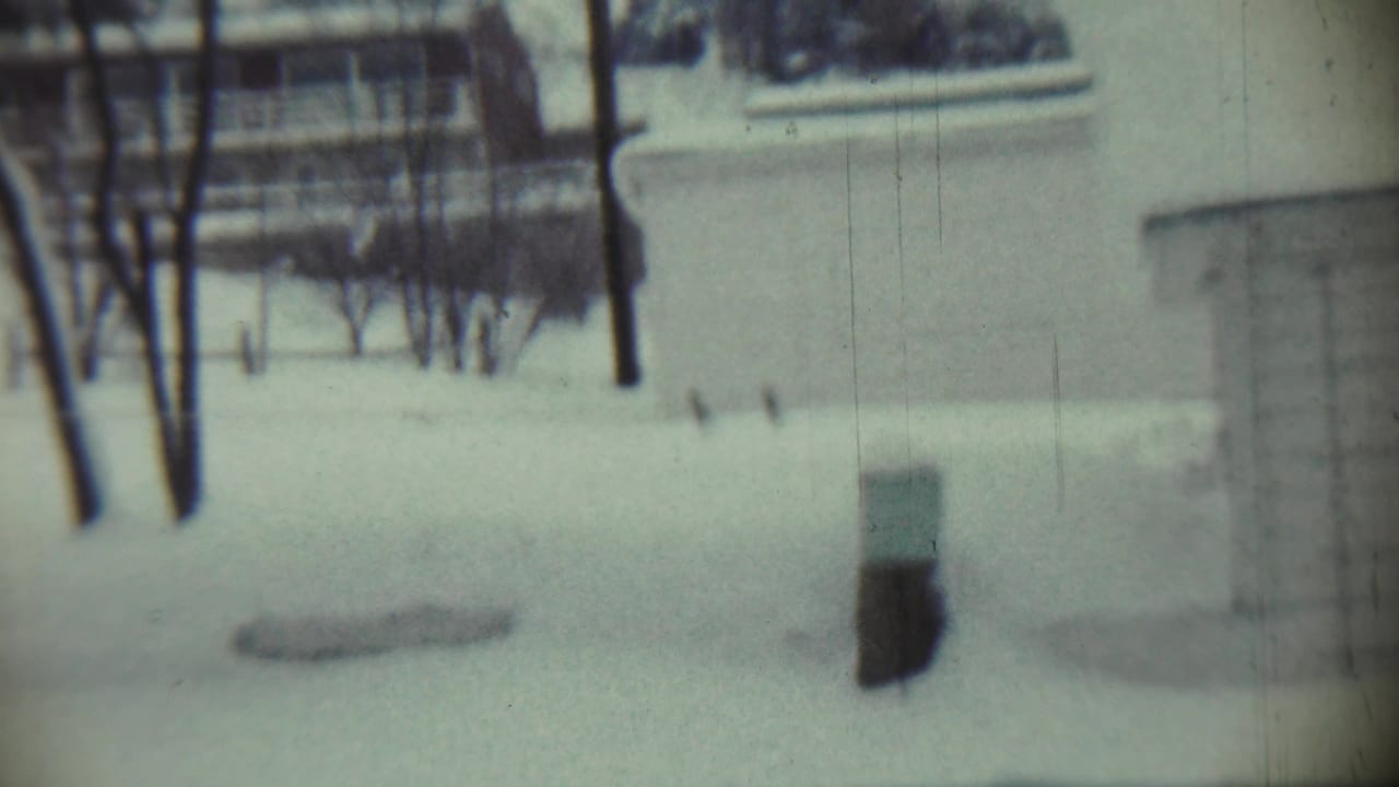 1959 Chadron, Nebraska home-movie frame showing a snow-covered residential lawn, bare trees, and part of a house beyond the yard.