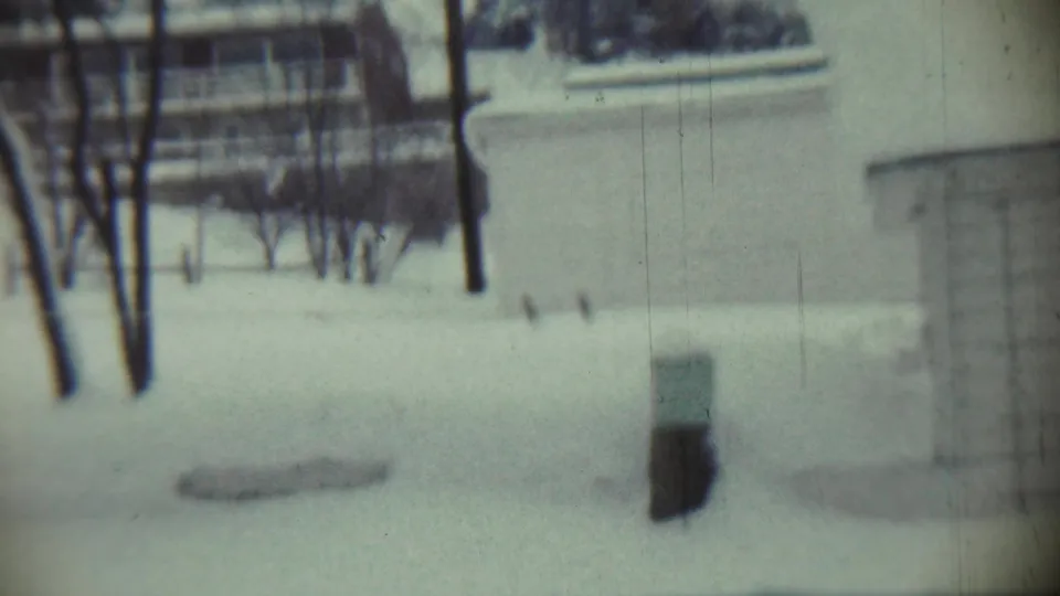 1959 Chadron, Nebraska home-movie frame showing a snow-covered residential lawn, bare trees, and part of a house beyond the yard.