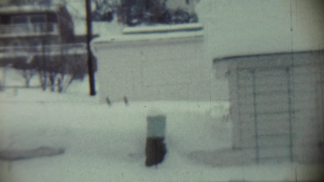 Snowy yard with a small post, house wall, and porch or entry structure.