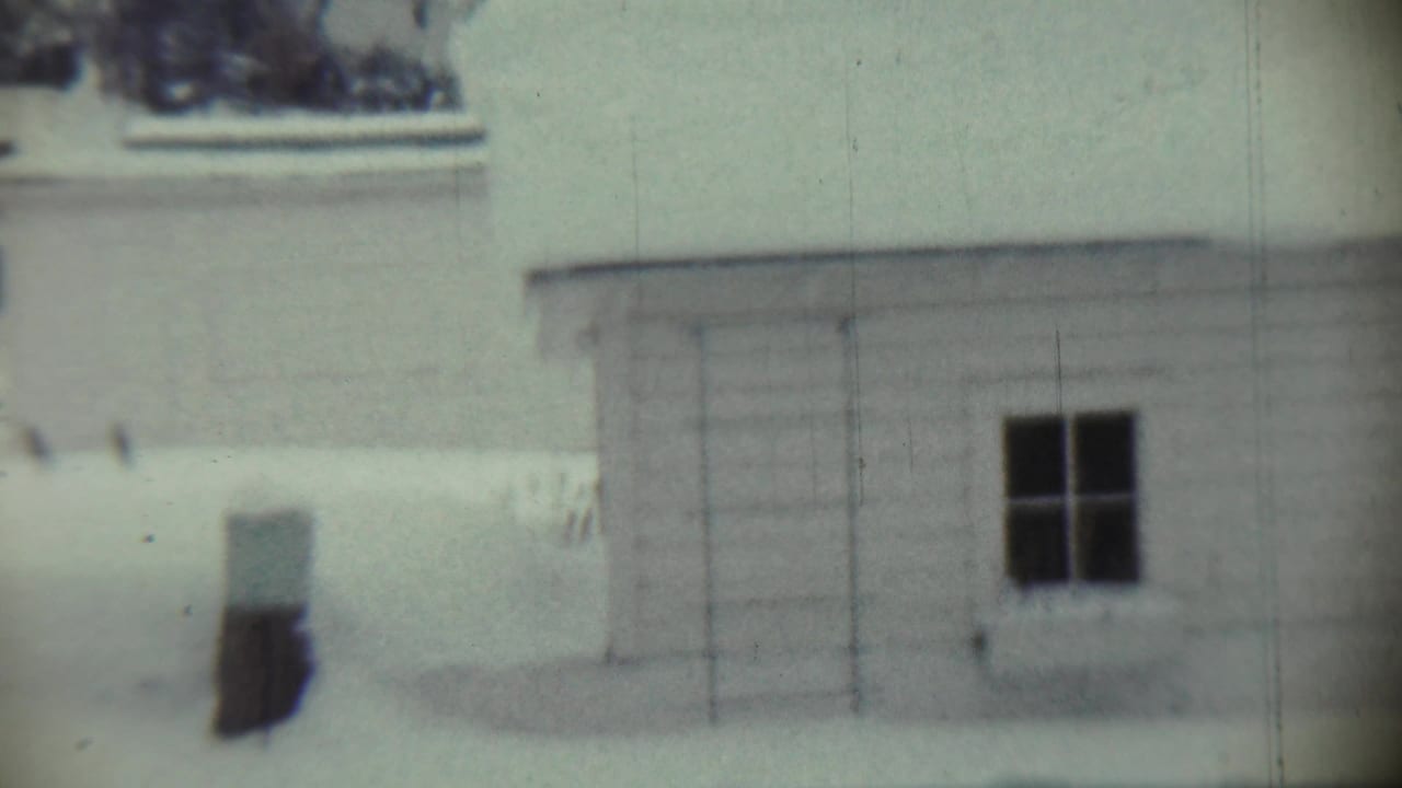 1959 Chadron, Nebraska 8mm frame showing a snow-covered white house exterior with a dark window and soft focus.
