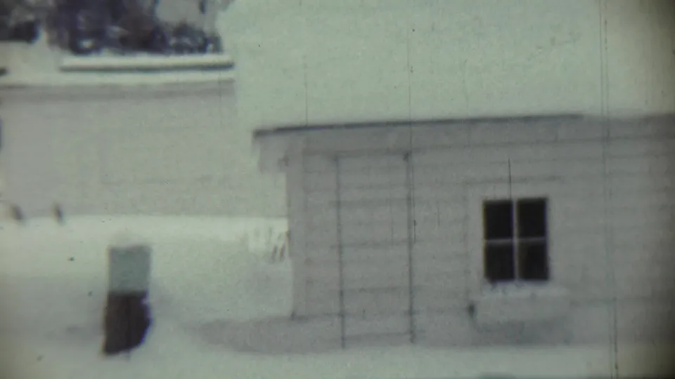 1959 Chadron, Nebraska 8mm frame showing a snow-covered white house exterior with a dark window and soft focus.