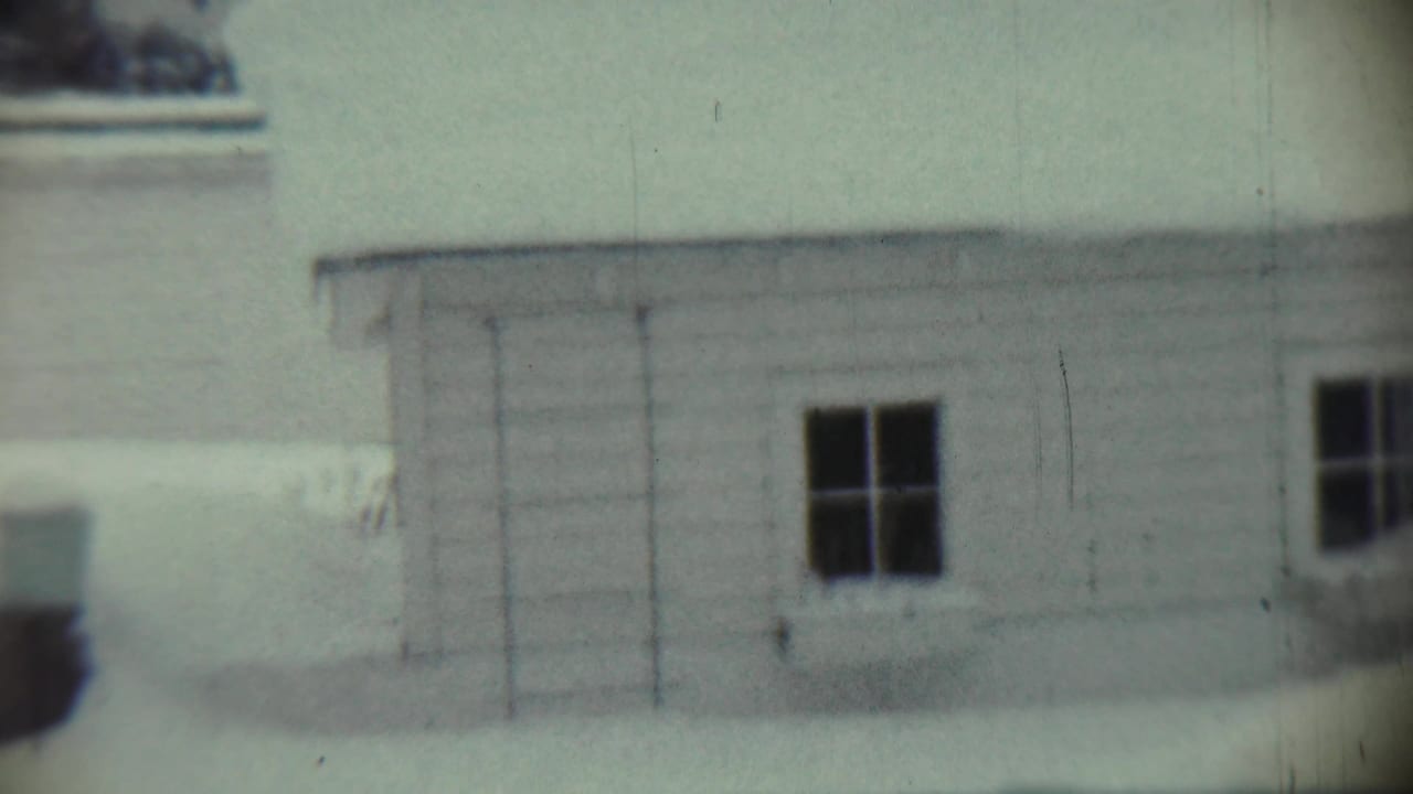 White house wall in snow with a dark window and blurred object near the side.