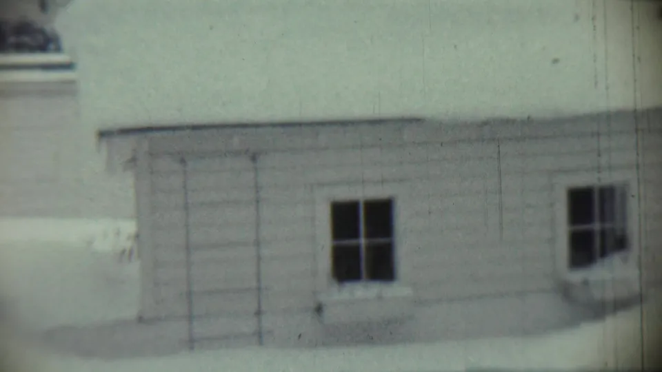 1959 Chadron, Nebraska 8mm frame showing the side of a snow-covered house with white siding and dark windows.