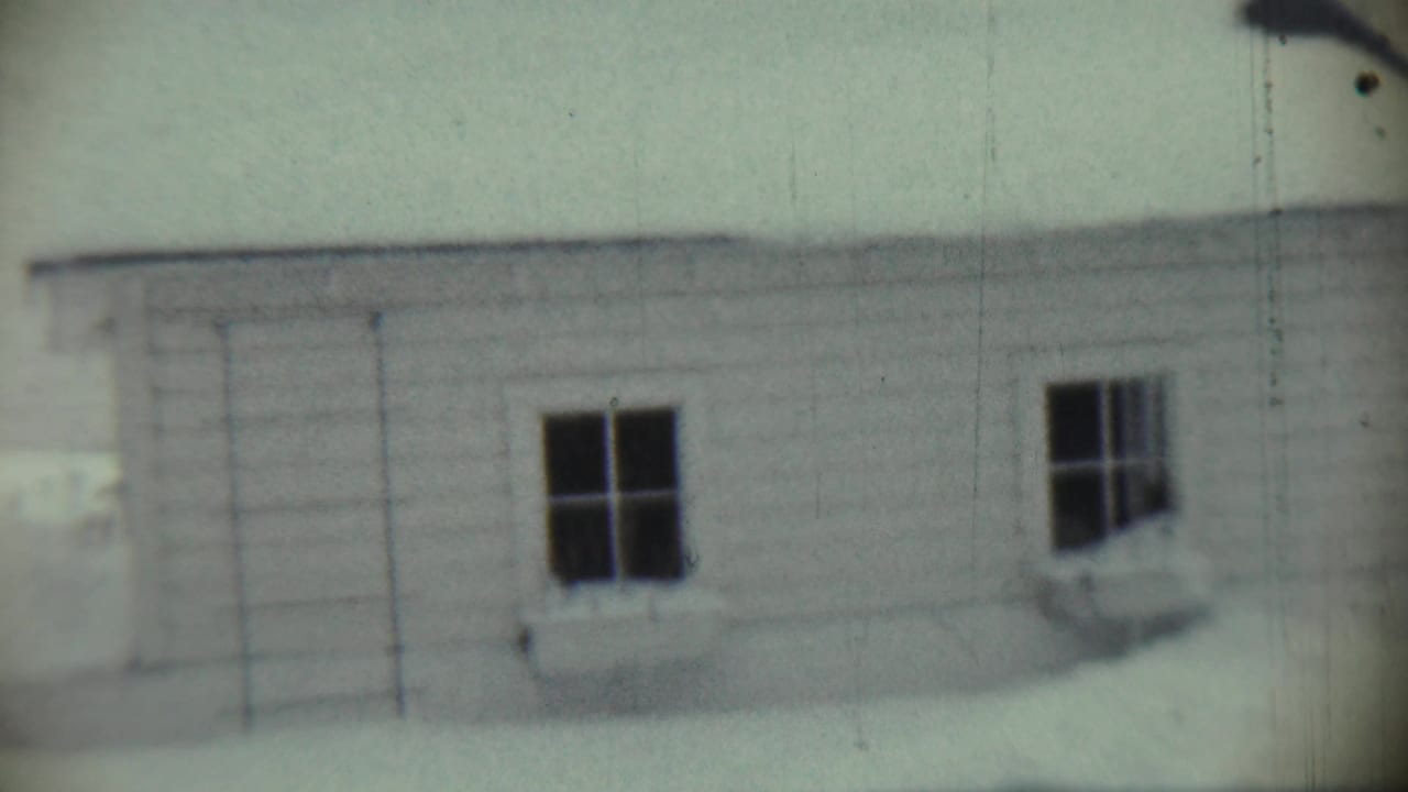 1959 Chadron, Nebraska 8mm frame showing snow-covered residential buildings with siding, dark windows, and a pale sky.