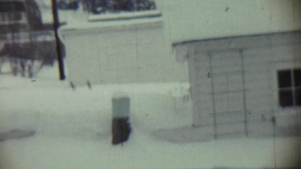 1959 Chadron, Nebraska 8mm frame showing a utility pole, bare trees, snow-covered ground, and a residential wall with a dark window.