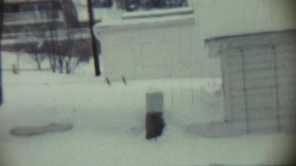 1959 Chadron, Nebraska 8mm frame showing bare trees and a utility pole near a snow-covered residential building with siding and a window.