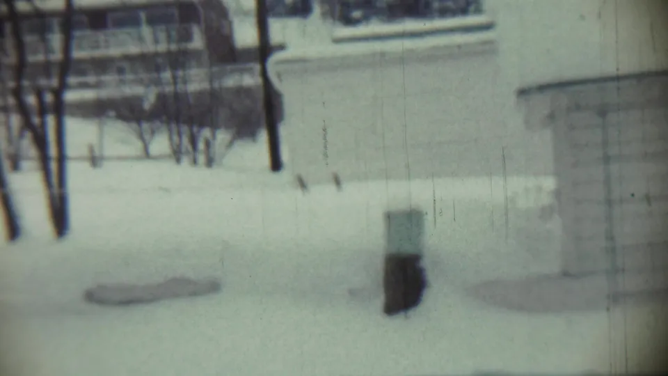 1959 Chadron, Nebraska home-movie frame showing a snowy backyard with bare trees, soft focus, and a building beyond the yard.