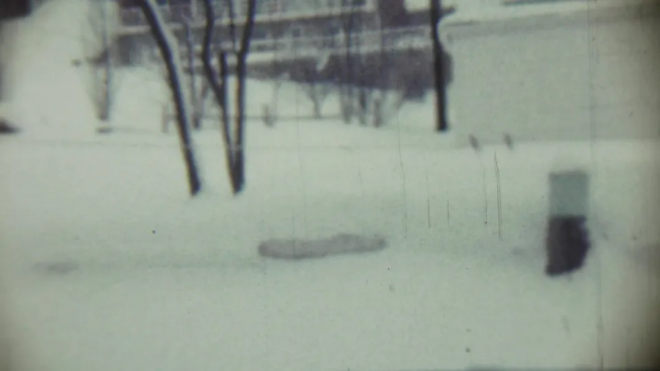 Snow-covered Chadron residential exterior with bare trees, a pale house wall, and darkened film-edge shadow from the 8mm scan.