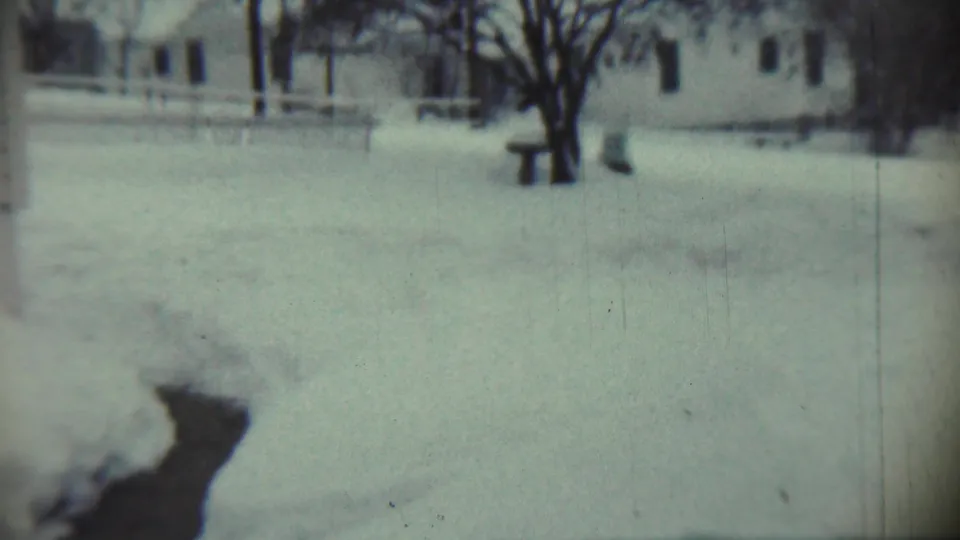 1959 Chadron, Nebraska 8mm frame showing a soft handheld view of snow drifts, a house, fence, bare trees, and an icy channel.