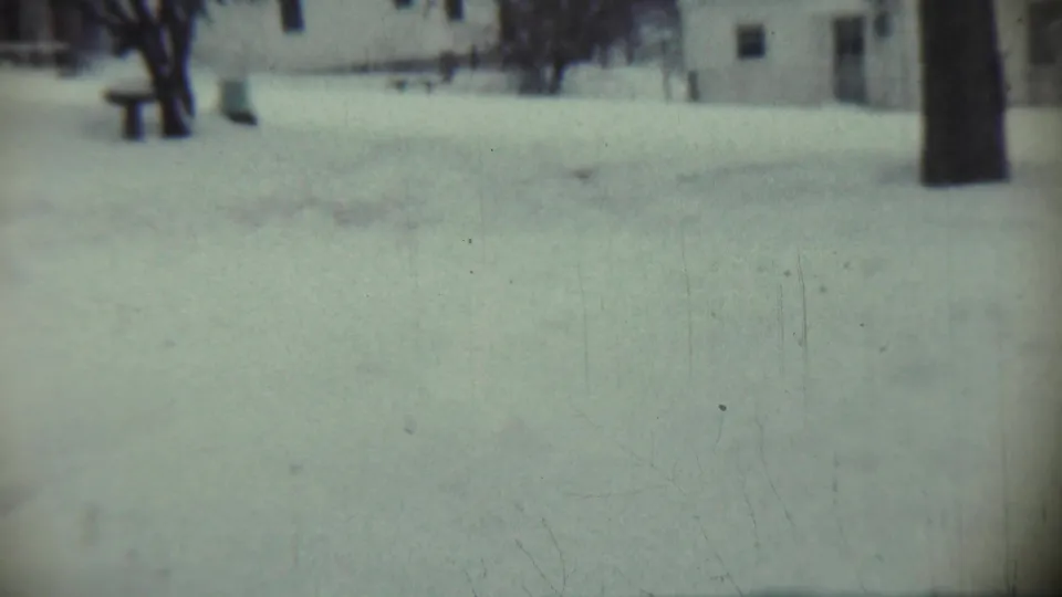 1959 Chadron, Nebraska frame of a snow-covered yard with bare trees, a right-edge trunk, and a house in soft background focus.