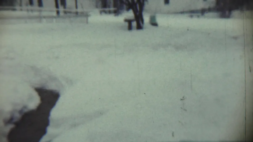 Final 1959 Chadron, Nebraska frame showing a blurred snow-covered yard, dark foreground shape, bare trees, and a distant house.