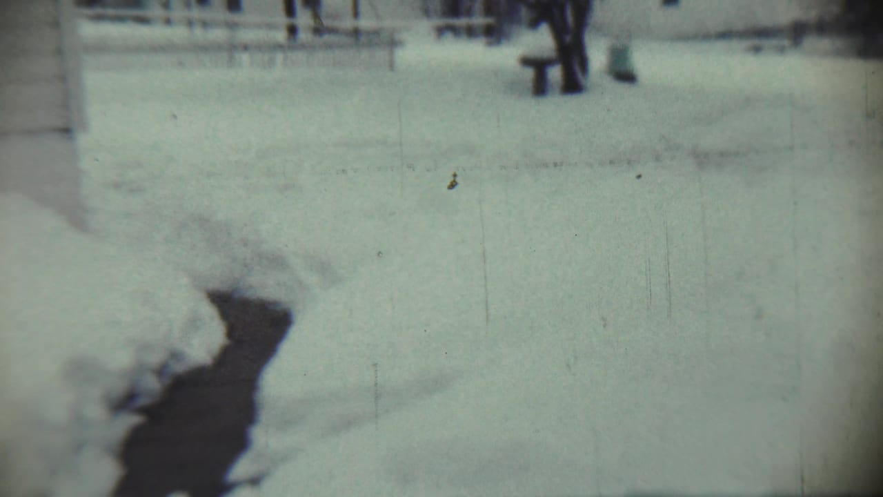 Snowy yard in Chadron, Nebraska, with a dark path or shadow visible across the winter ground in 1959 home-movie footage.