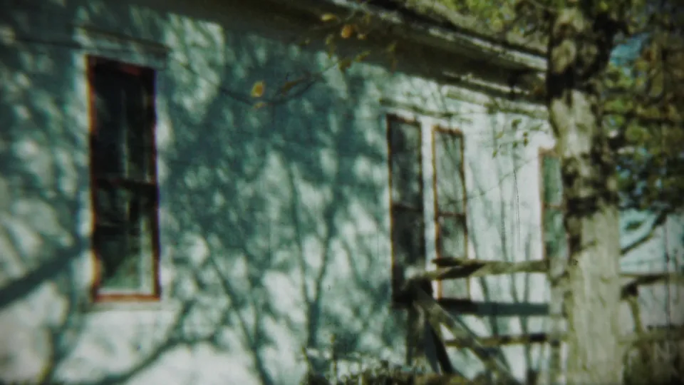 1959 Chadron, Nebraska view of a white house side wall with windows, tree trunk, and wind-blown foliage shadows.