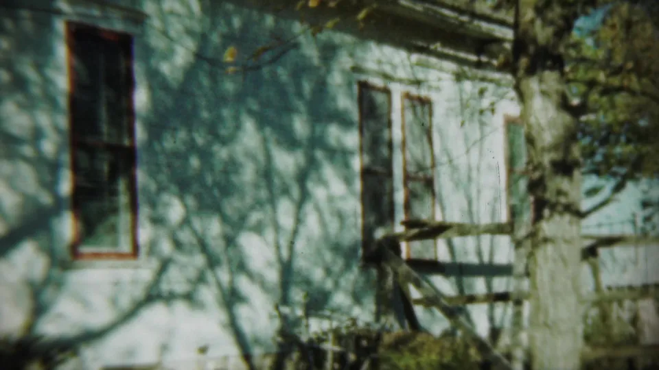 1959 Chadron, Nebraska frame showing the side of a white house with windows, a tree trunk, and shifting branch shadows.