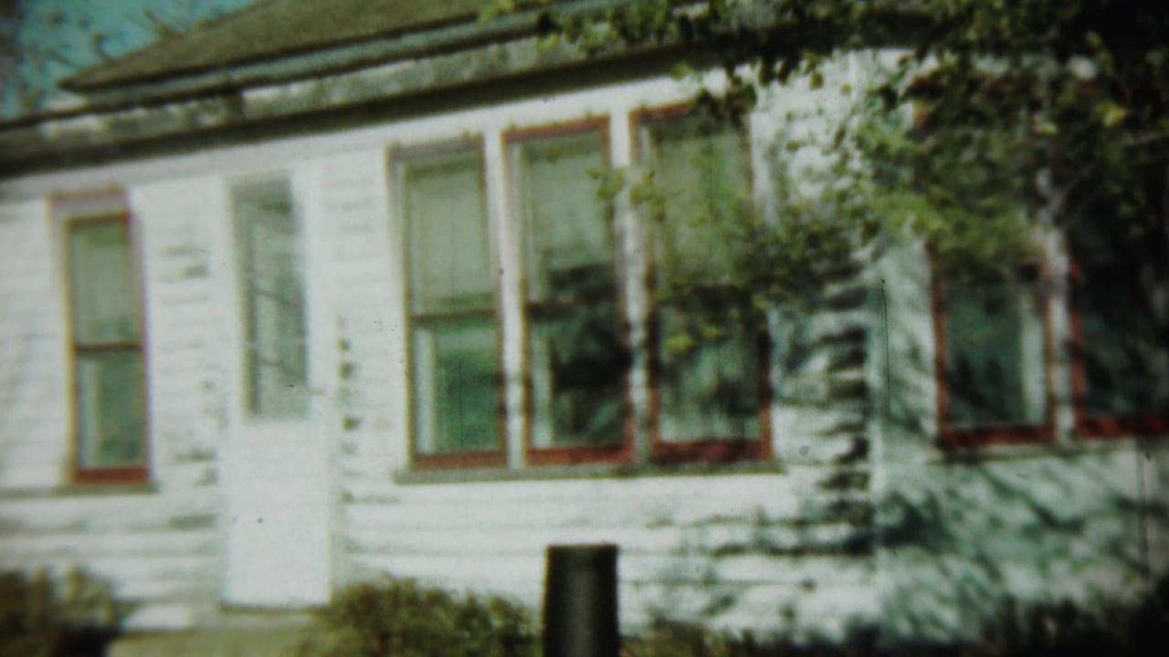 White clapboard house with red-trimmed windows, a white door, and tree shadows across the facade.