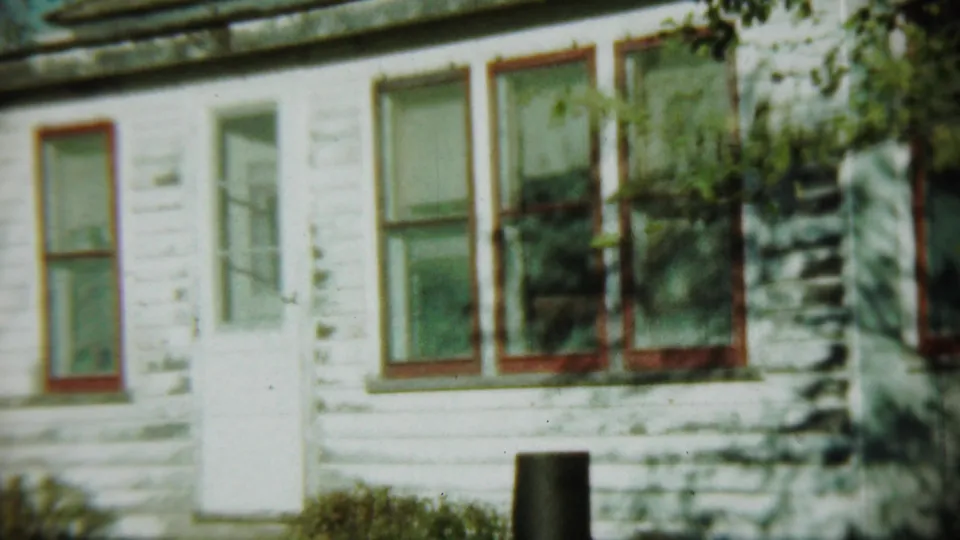 1959 Chadron, Nebraska 8mm view of a white clapboard house facade with red trim and weathered exterior paint.