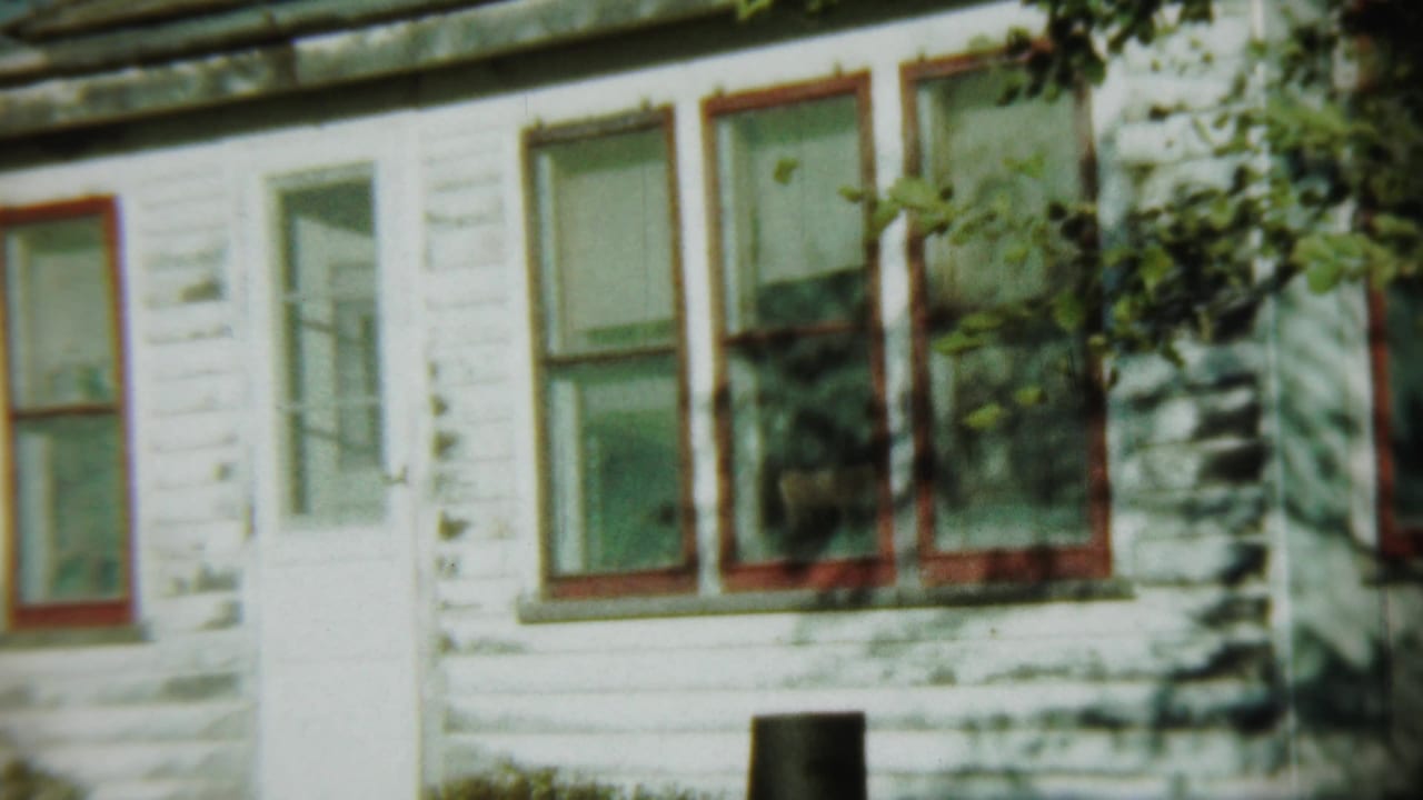White clapboard house exterior with red-trimmed windows and a white door partly shaded by foliage.