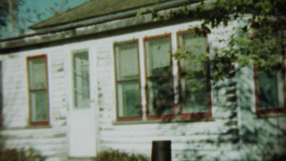 1959 Chadron, Nebraska home-movie still showing the same weathered house front, with red-trimmed windows, a white door and yard vegetation.