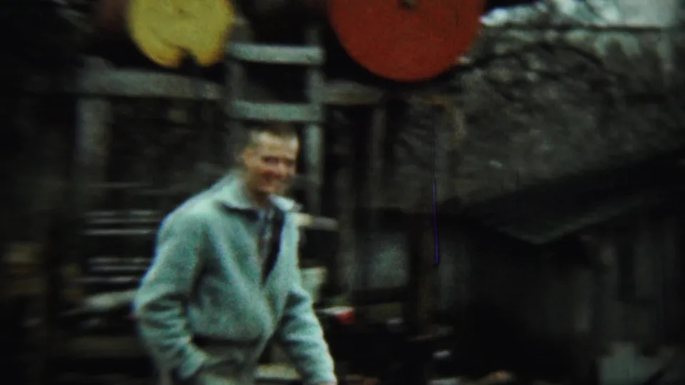 1959 Chadron, Nebraska home-movie frame showing a man near large barrels, a ladder, and farm structures.