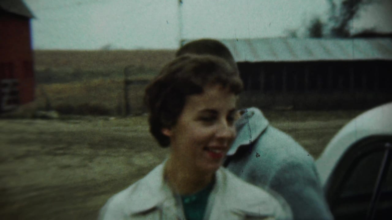 In 1959 Chadron, Nebraska footage, a young woman in a white coat smiles in a farmyard with cars, a red barn, and open fields behind her.