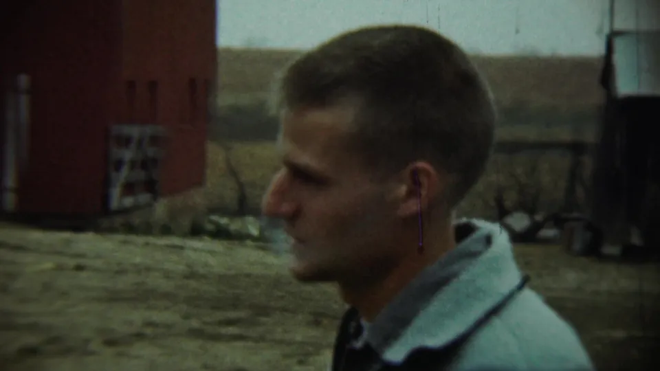 The final frame shows a close side view of a man in a light jacket, with a red barn, shed, fence, and muted rural Nebraska landscape behind him.