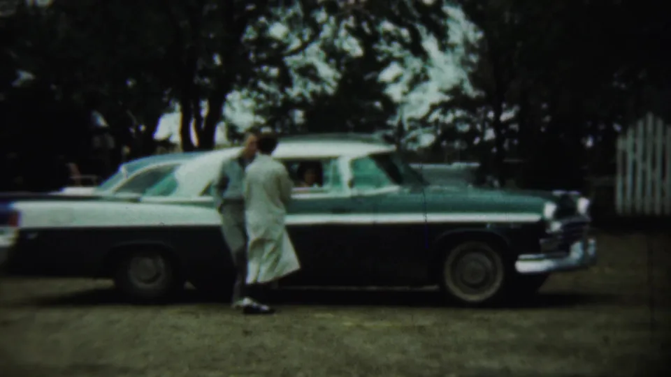 In the 1959 Chadron, Nebraska footage, the couple stands by the sedan while a passenger is visible through the open window.