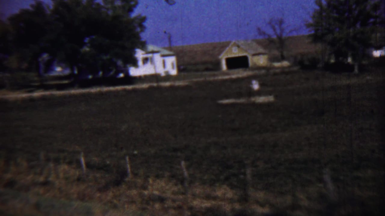 Distant farmhouse and barn across an open field under a dark blue sky.