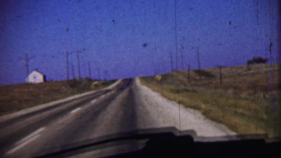 A rural road in 1959 Cheyenne County, Kansas stretches ahead between open fields, utility poles, and a small roadside building.