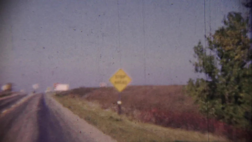 1959 Cheyenne County, Kansas highway view with a yellow warning sign, open fields, grassy roadside, distant traffic, and a tree line.