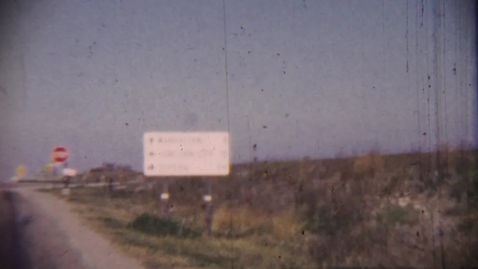 1959 Cheyenne County, Kansas roadside view with a red stop sign, white direction sign, grassy embankment, and open sky.