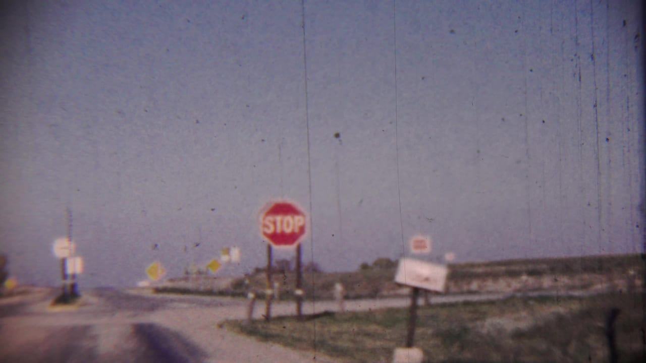 Rural intersection with a red stop sign beside a paved road and open fields.