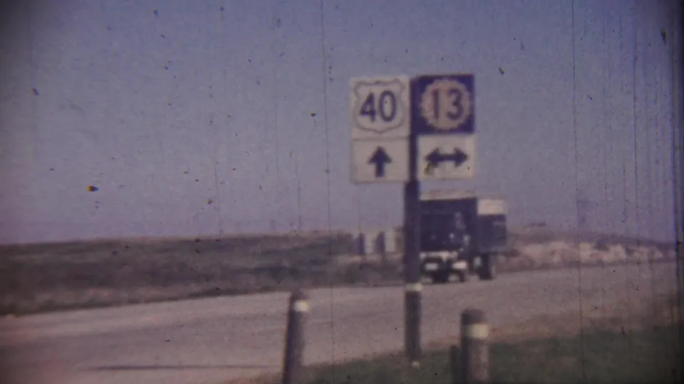 1959 rural Kansas highway-sign view with route 40 and 13 markers, arrow signs, roadside posts, and a truck beyond the signpost.