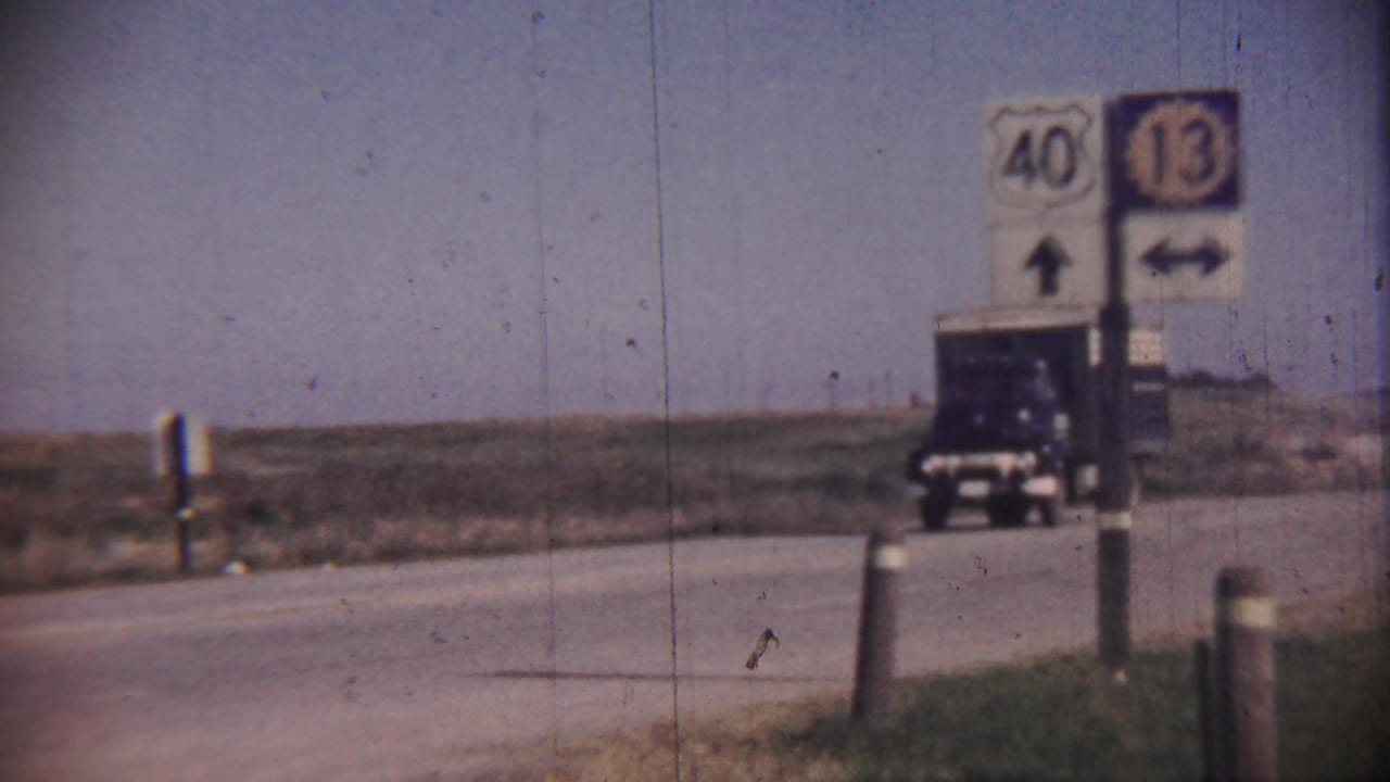 A dark blue cargo truck travels along a rural highway in Cheyenne County, Kansas, with route signs for 40 and 13 visible near the roadside.