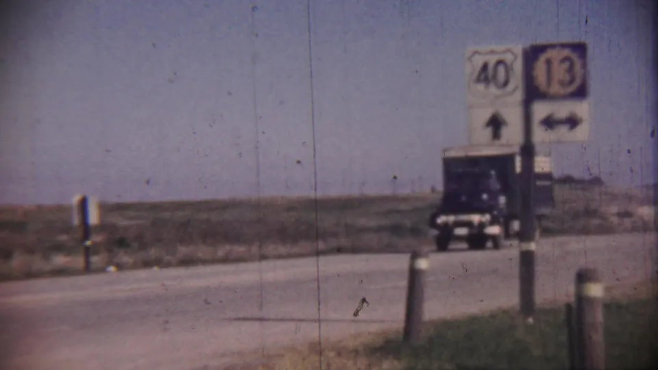 A dark blue cargo truck travels along a rural highway in Cheyenne County, Kansas, with route signs for 40 and 13 visible near the roadside.