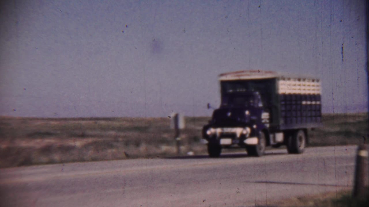Dark truck with cargo body drives along an open rural highway.