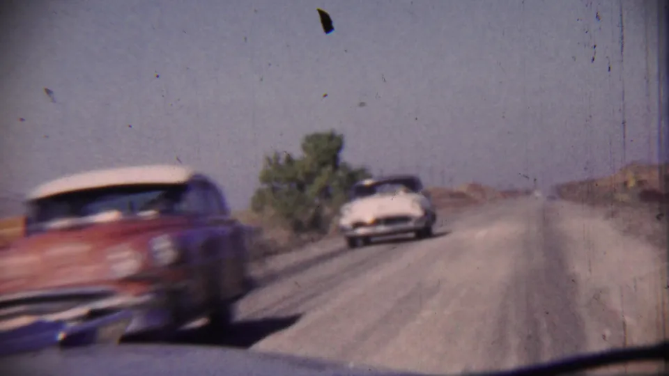 1959 Cheyenne County, Kansas road view with a red and white car passing close to the camera and a white sedan approaching in the distance.