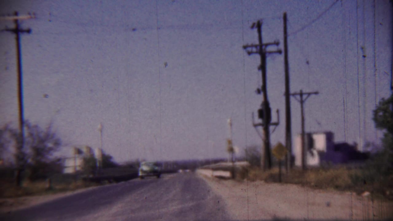 Open highway with utility poles, roadside structures, and a distant vehicle ahead.