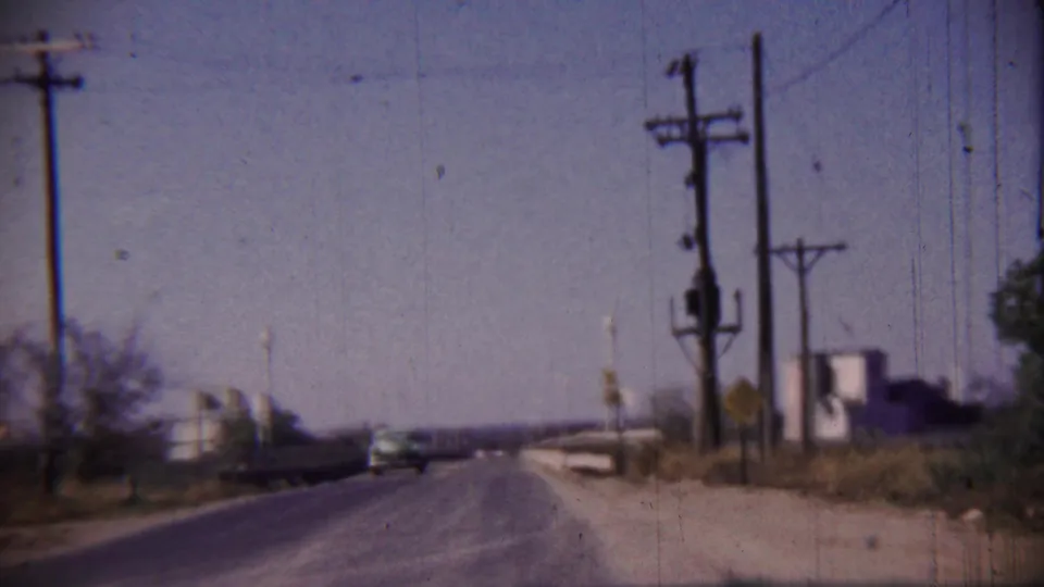 Rural Cheyenne County, Kansas highway scene from a moving vehicle, with utility poles, roadside signs, and a distant car under a clear sky.
