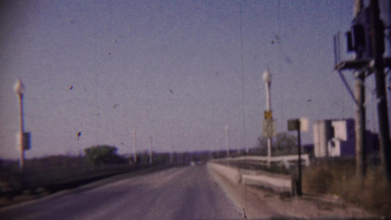 Forward view on a two-lane bridge with railings, street lamps, and a roadside speed sign.