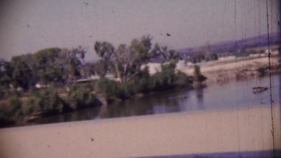 1959 Cheyenne County, Kansas frame showing river water, dense trees, a bridge parapet, and distant low hills.