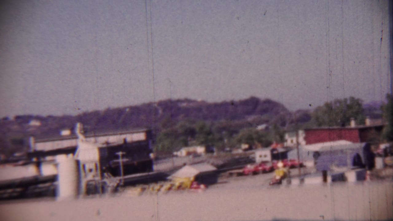 1959 Cheyenne County, Kansas street view with low commercial buildings, parked cars, distant hills, and a roadside service area.