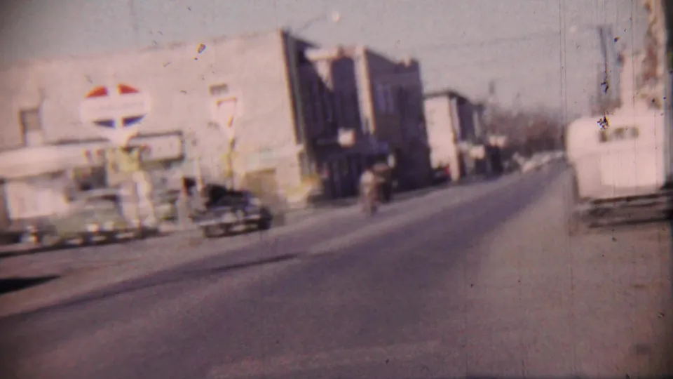 1959 Cheyenne County street scene with a visible Standard Oil sign, period cars, storefronts, and motion blur from the moving camera.
