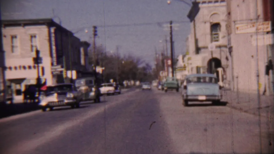 1959 Cheyenne County, Kansas street scene with parked and moving cars, traffic signals, utility poles, and two-story buildings.