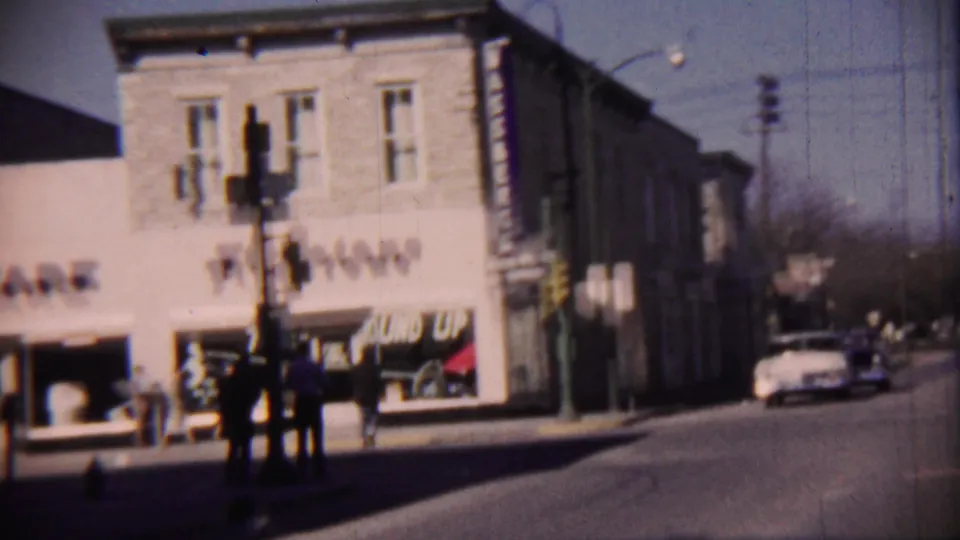 Cheyenne County, Kansas street corner with Firestone storefront signage, pedestrians on the sidewalk, a traffic signal, and mid-century cars.