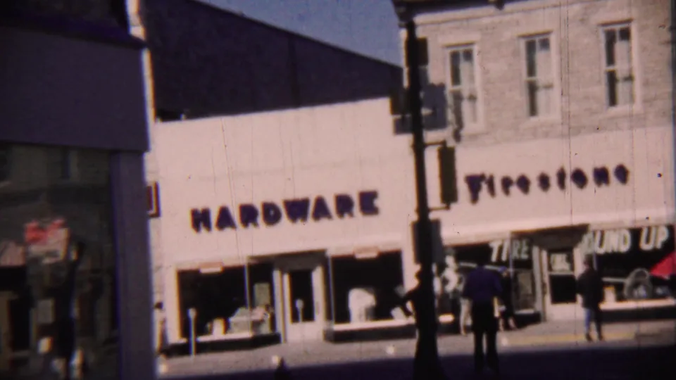 1959 8mm frame showing hardware lettering beside a Firestone tire shop on a Cheyenne County, Kansas commercial block.