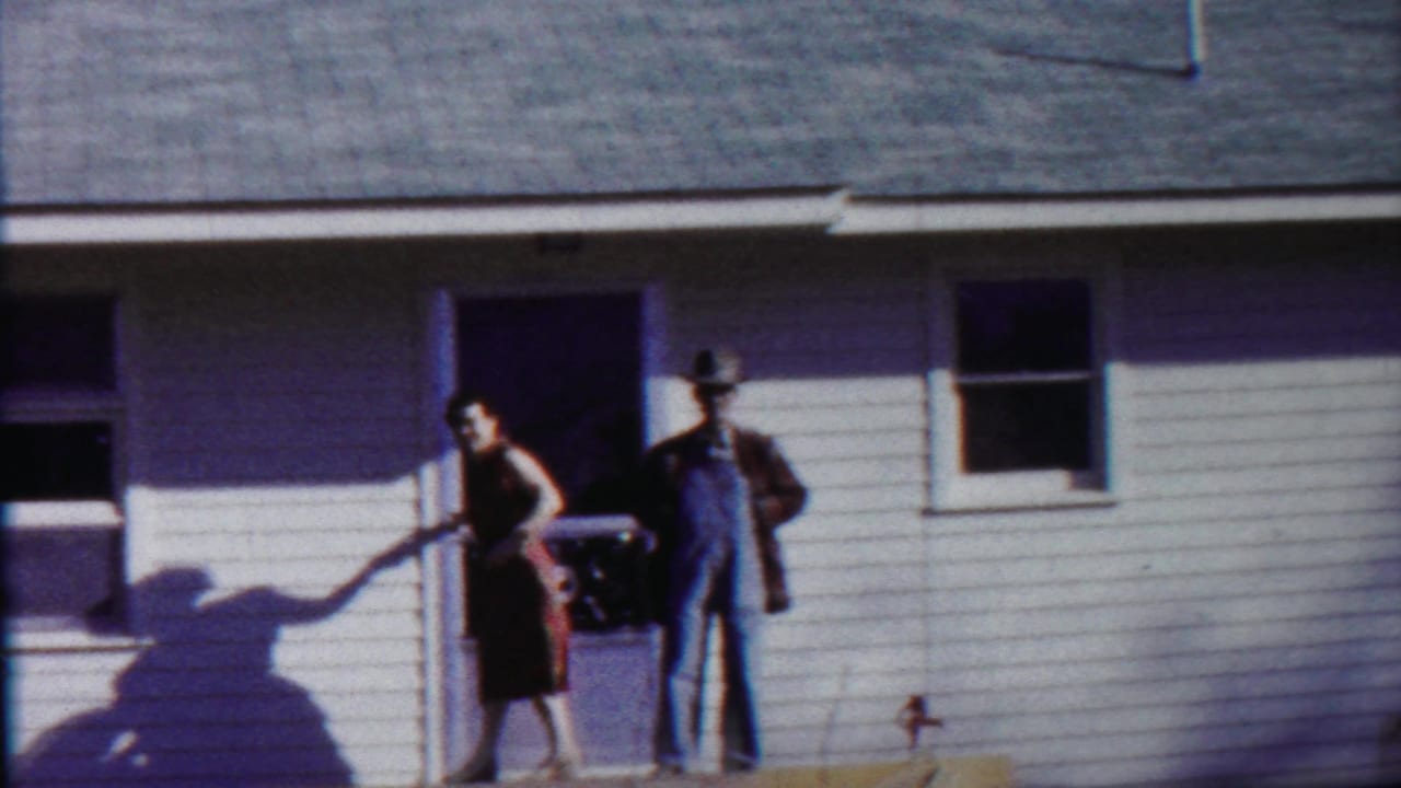 Woman in a dark dress stands beside a man in overalls near the porch door.