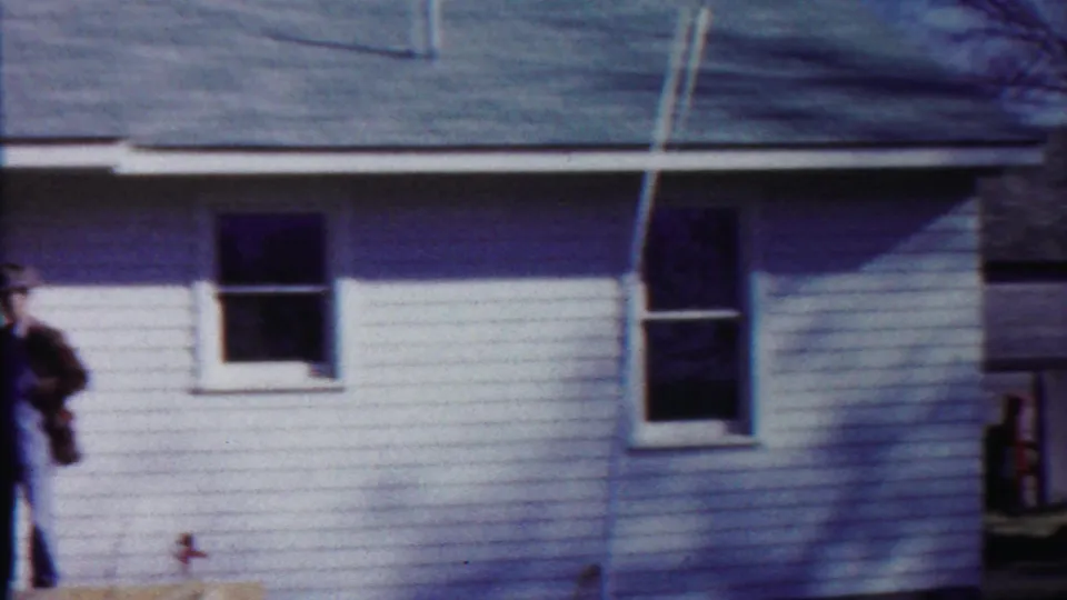 A man in overalls and a hat stands alone near the doorway of the Saint Francis house as the porch scene ends.