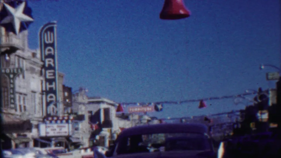 1959 Saint Francis street view with the Wareham theater sign, hotel sign, classic cars, and overhead red bell decorations.