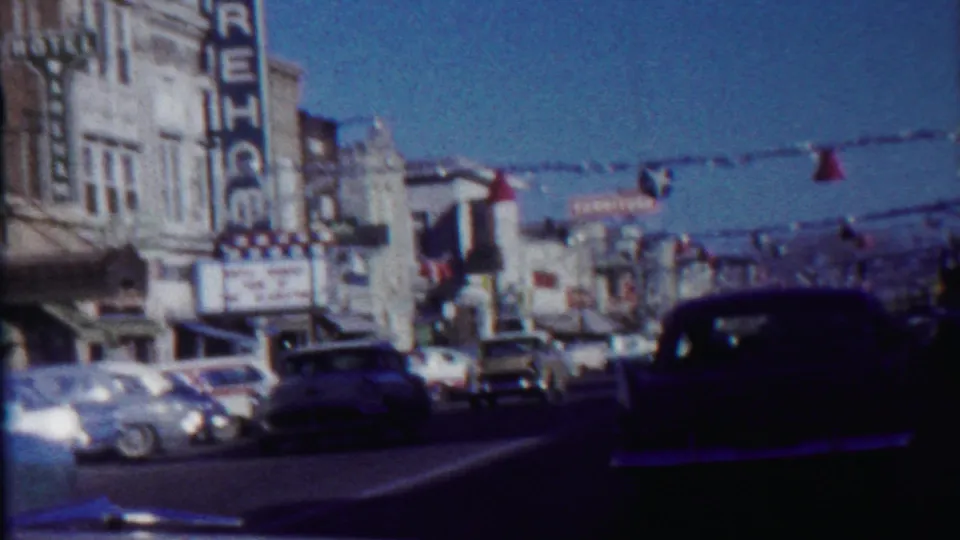 1959 Saint Francis, Kansas street view with classic cars, a theater marquee, storefronts, and overhead red and blue streamers.